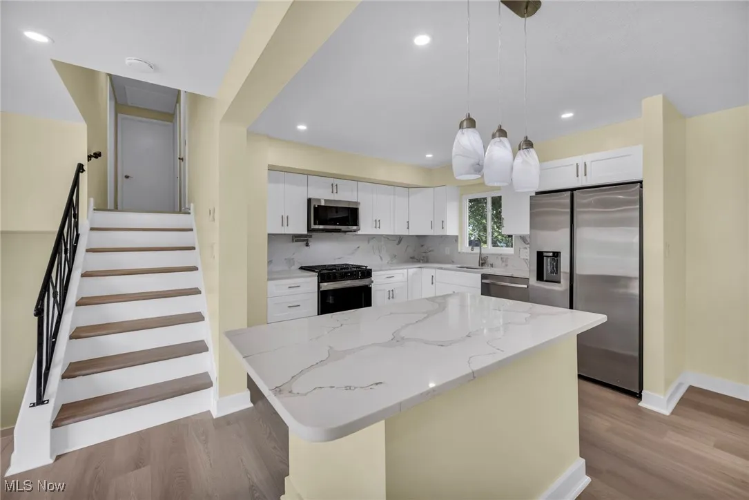 Kitchen with stainless steel appliances, wood finished floors, tasteful backsplash, light stone counters, and pendant lighting