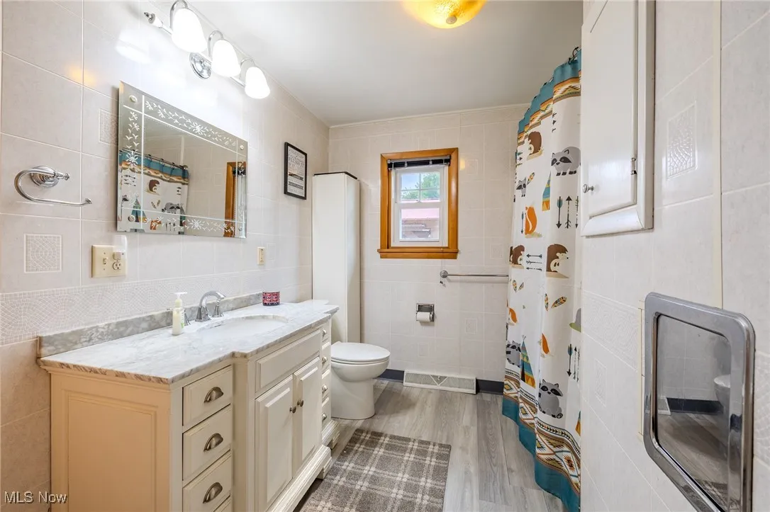 Full bath featuring tile walls, vanity, wood finished floors, and a shower with shower curtain