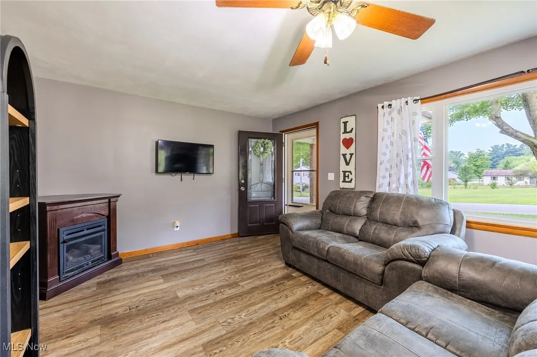 Living room with light wood-style floors, a glass covered fireplace, and a ceiling fan