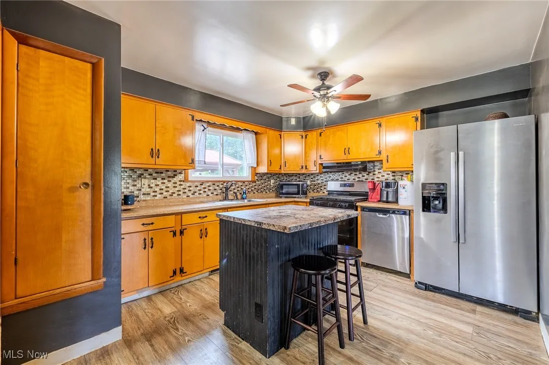 Kitchen featuring appliances with stainless steel finishes, decorative backsplash, light wood-style floors, and a kitchen island