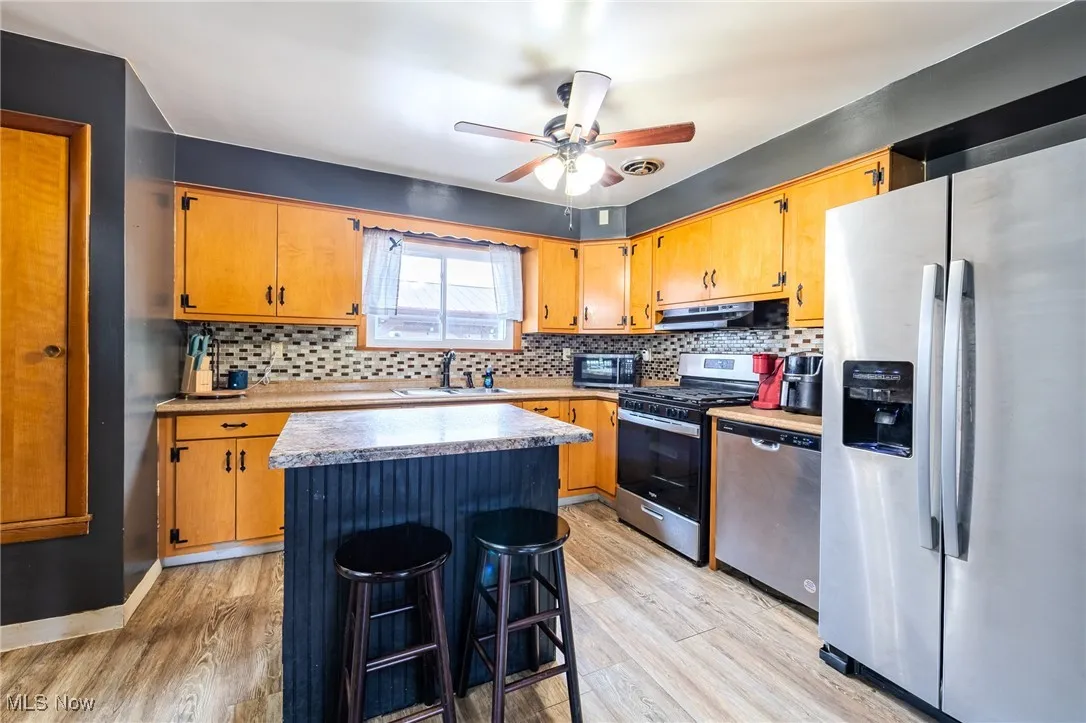 Kitchen featuring stainless steel appliances, decorative backsplash, light wood-style floors, a center island, and under cabinet range hood