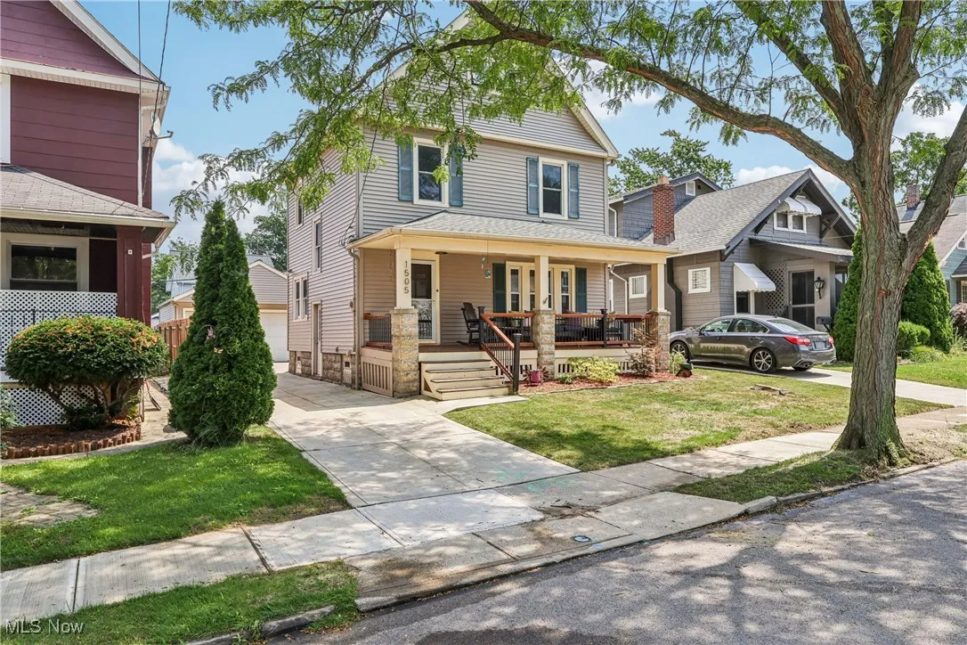 Traditional style home with a front yard, a garage, covered porch, and an outbuilding