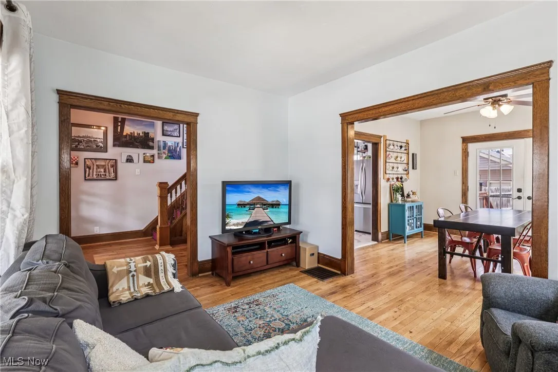 Living area with light wood-style flooring, ceiling fan, and stairway