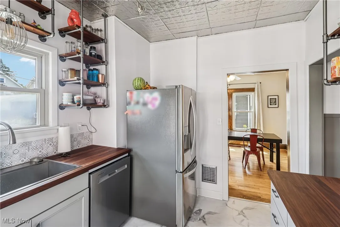 Kitchen with wood counters, stainless steel appliances, light marble finish flooring, an ornate ceiling