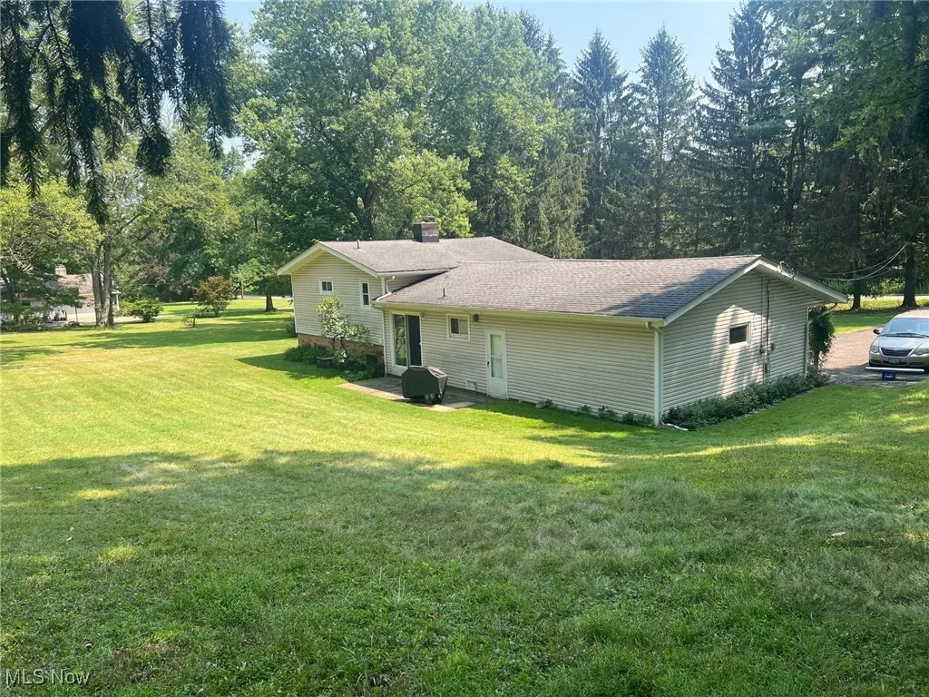 Rear view of house with a yard, patio area, and roof with shingles