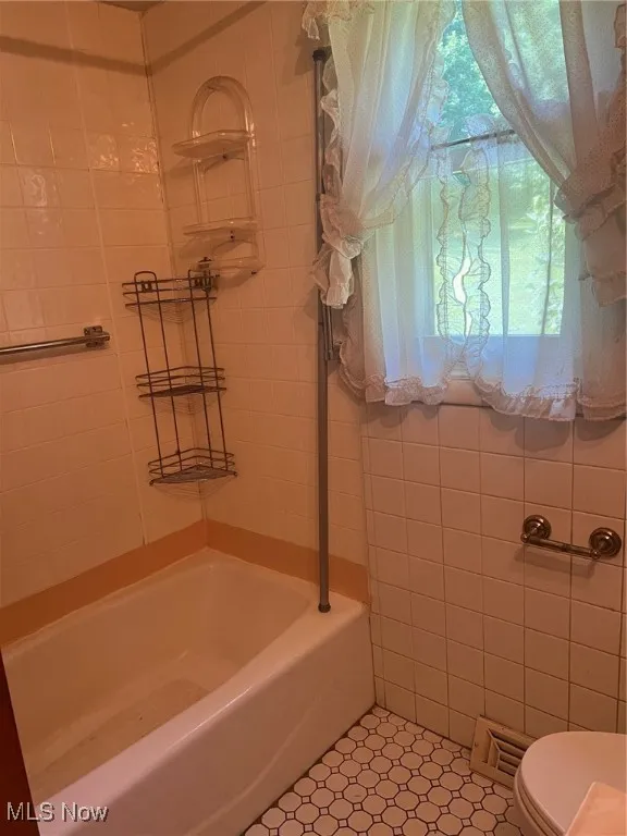 Bathroom featuring tile walls, washtub / shower combination, and tile flooring