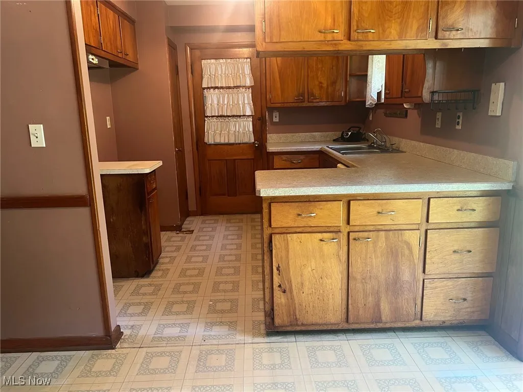 Kitchen featuring light flooring, brown cabinetry, light countertops, and a peninsula