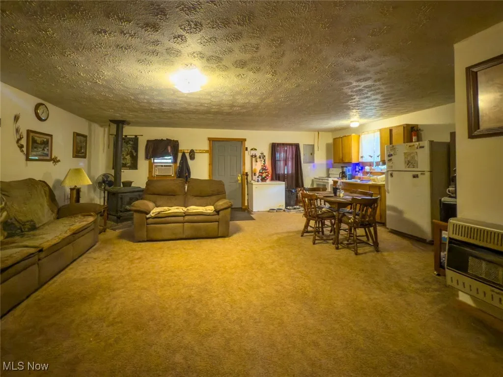 Living room featuring a wood stove, a textured ceiling, carpet floors, heating unit, and cooling unit