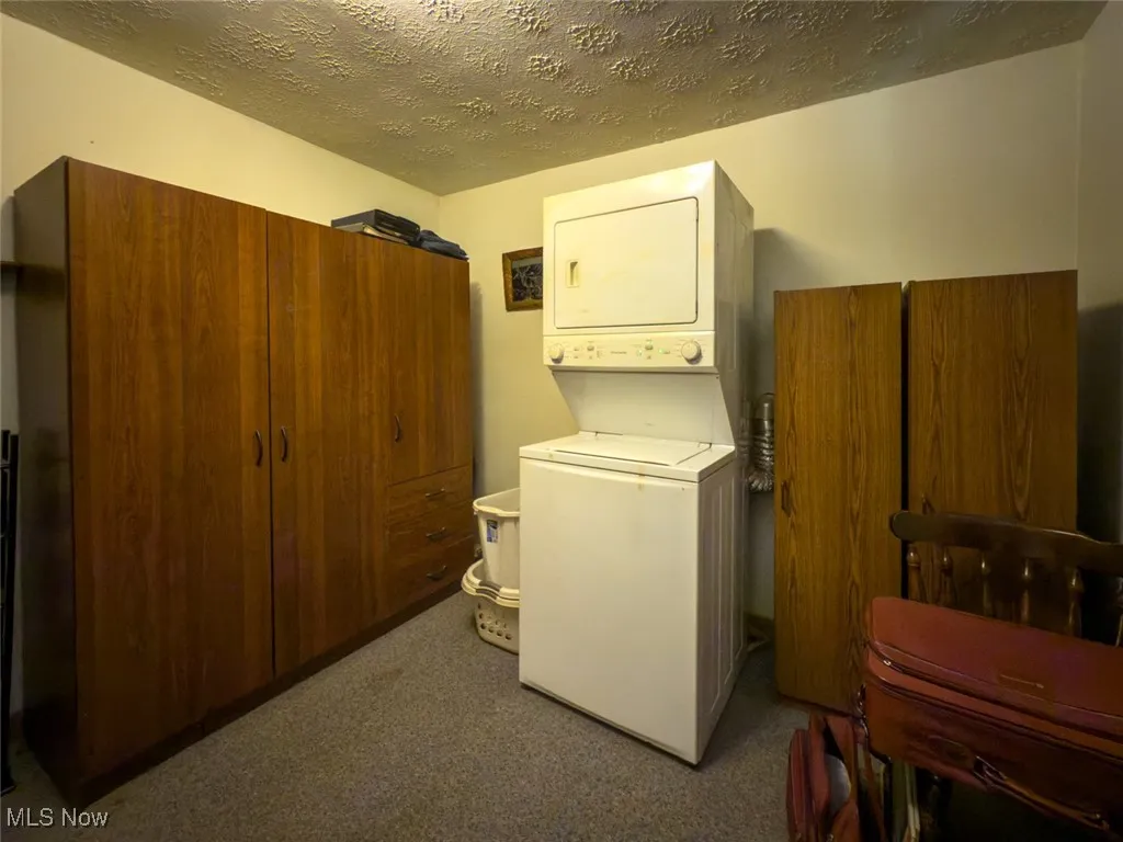Laundry area featuring stacked washer / dryer, a textured ceiling, and carpet flooring