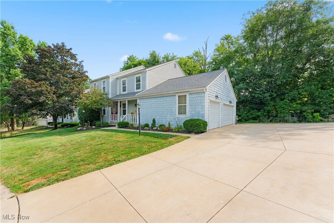 Traditional-style home featuring an attached garage, covered porch, a front yard, driveway, and roof with shingles