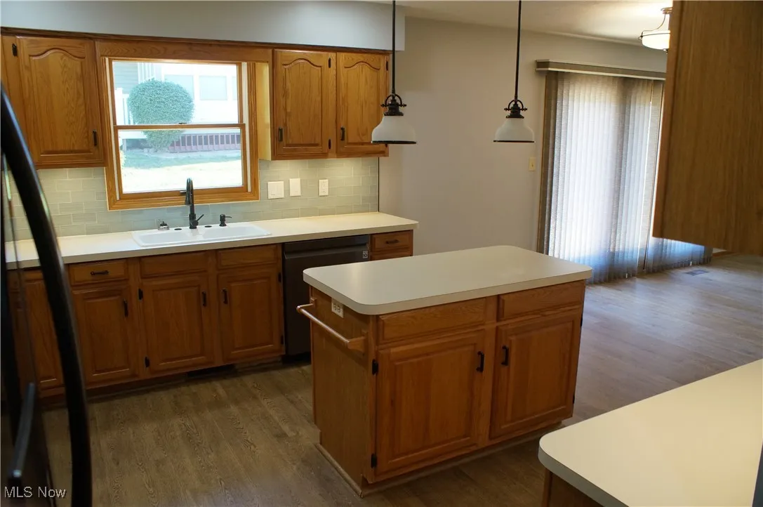 Kitchen with freestanding refrigerator, dark wood finished floors, light countertops, a center island, and dishwasher