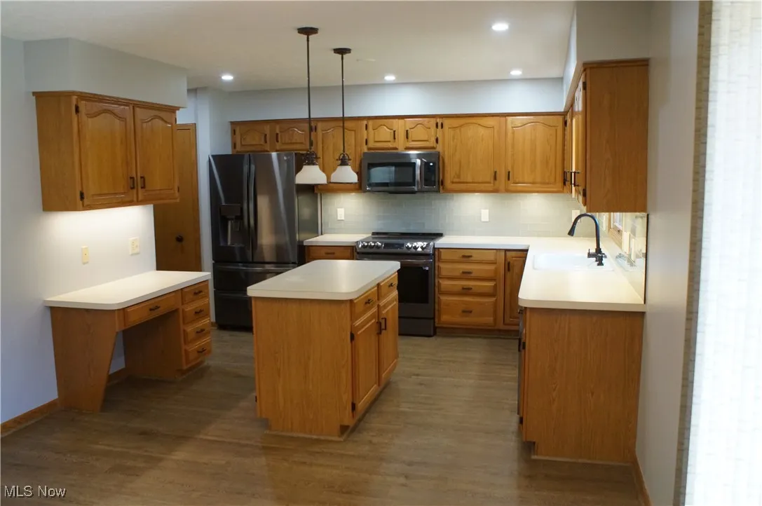 Kitchen with stainless steel appliances, a center island, backsplash, dark wood finished floors, and light countertops