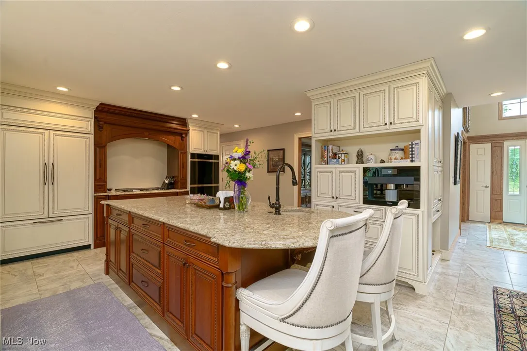 Kitchen featuring recessed lighting, open shelves, quartz counters, cream cabinetry, and a center island with sink