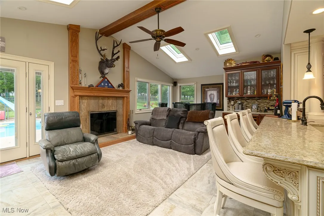 Sun room with beam ceiling, a tile fireplace, ceiling fan, a skylight, and high vaulted ceiling