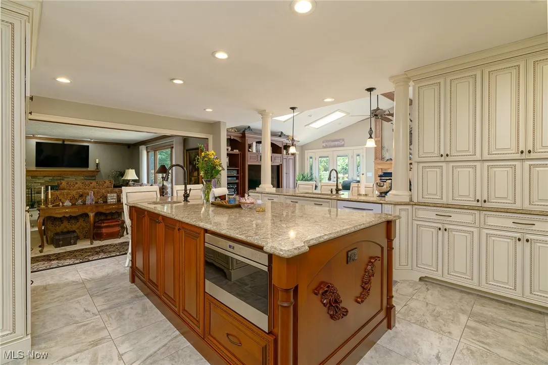 Kitchen with cream cabinetry, open floor plan, vaulted ceiling, quartz counters.