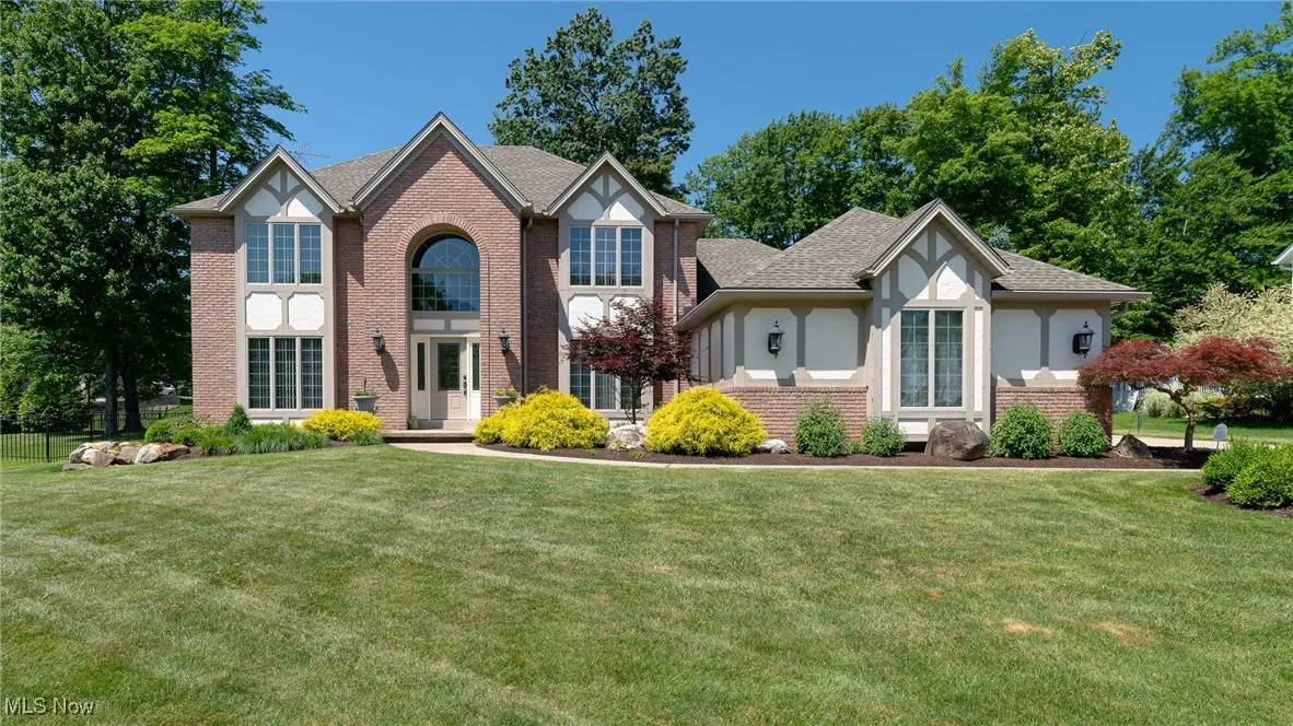 Tudor house featuring brick siding, a front lawn, stucco siding, and a shingled roof