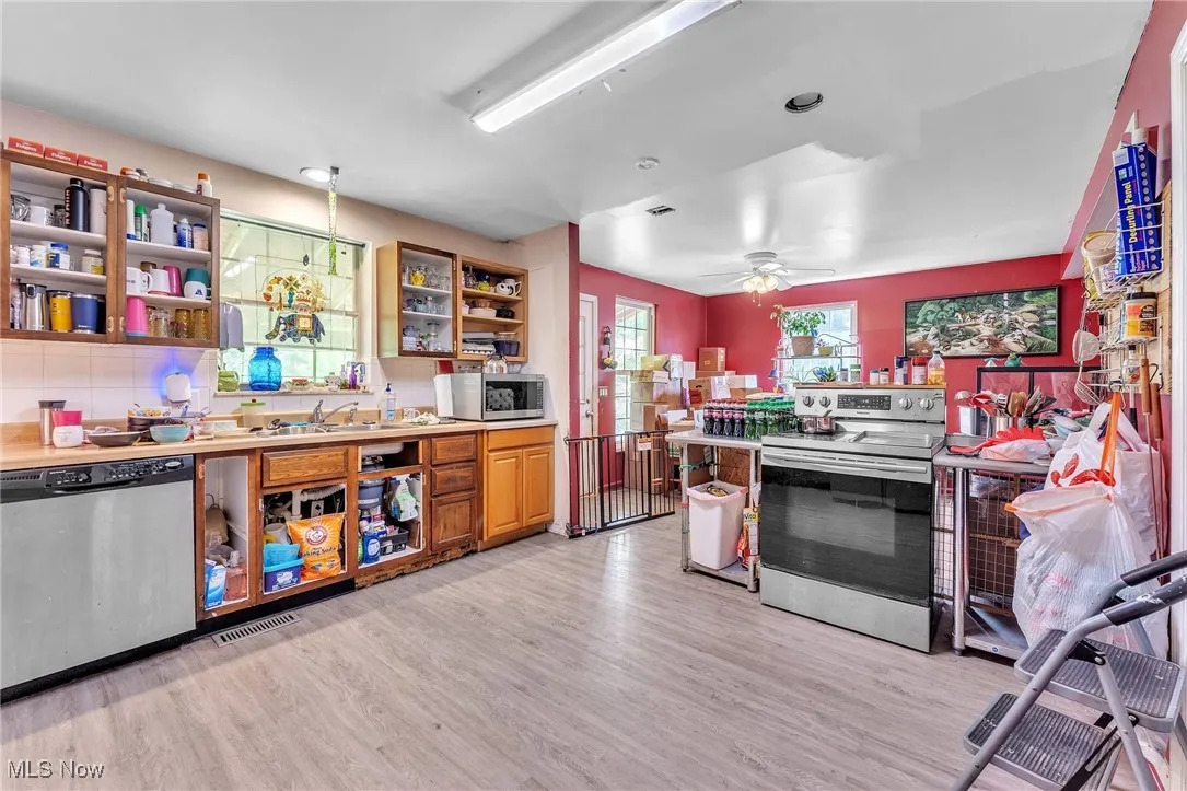 Kitchen featuring appliances with stainless steel finishes, open shelves, light wood-style floors, tasteful backsplash, and light countertops