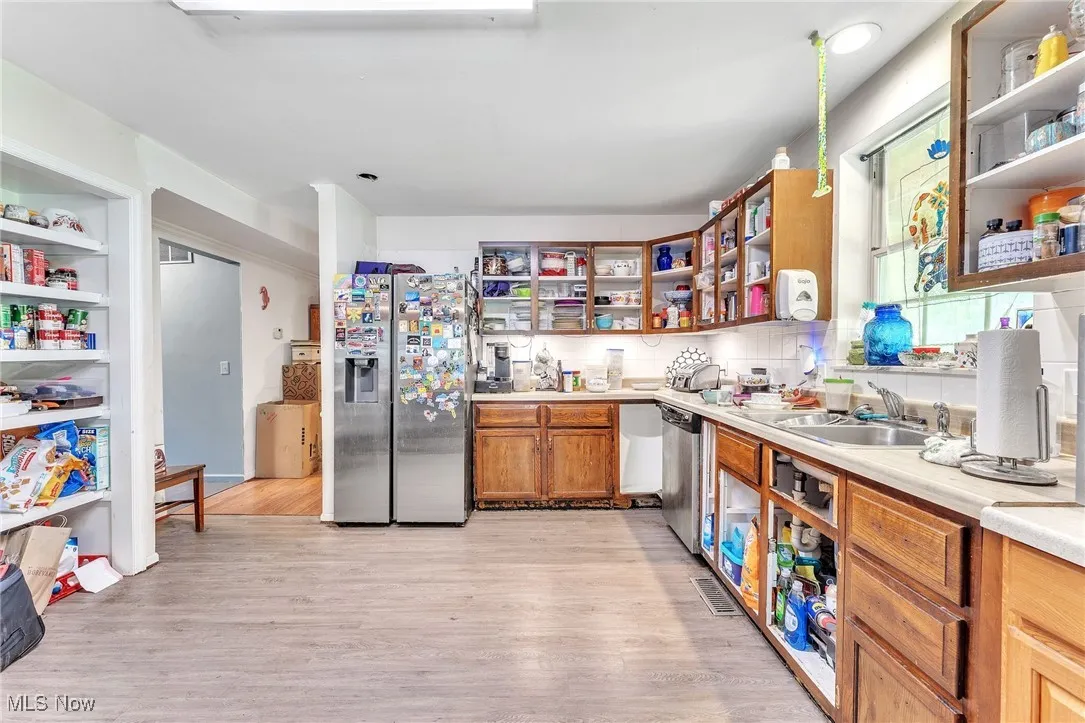 Kitchen with open shelves, light wood-style flooring, appliances with stainless steel finishes, and decorative backsplash