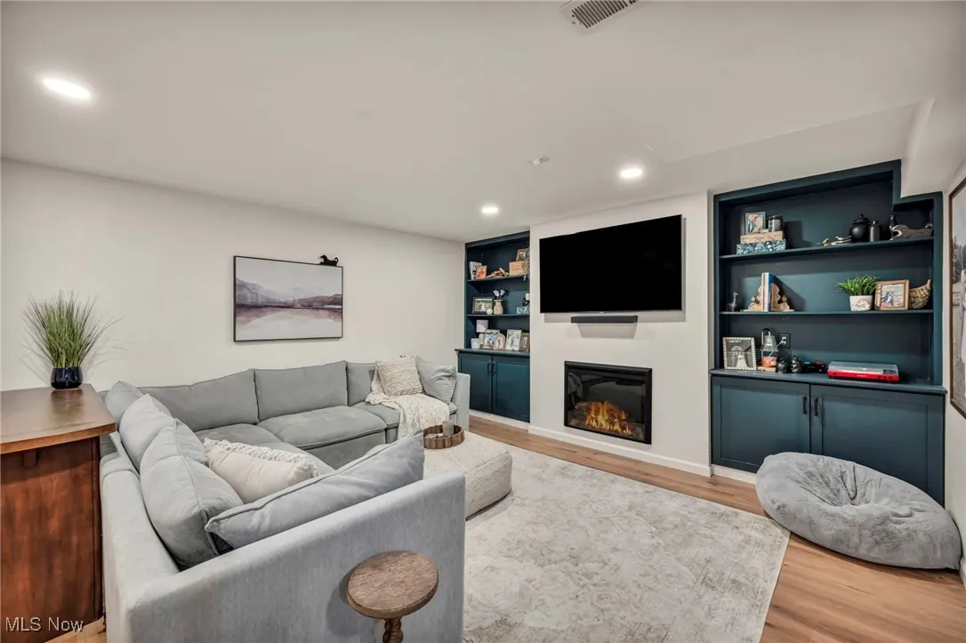 Recreation area featuring wood finished floors, recessed lighting, a glass covered fireplace, and built in features