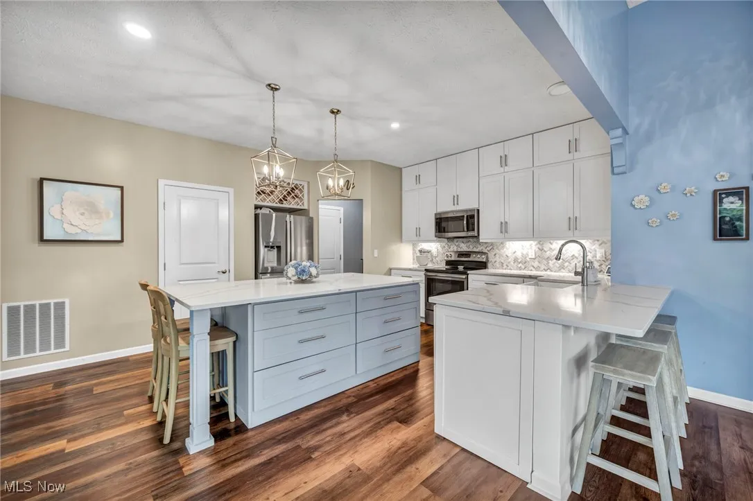 Kitchen with a breakfast bar area, appliances with stainless steel finishes, dark wood-style floors, white cabinetry,