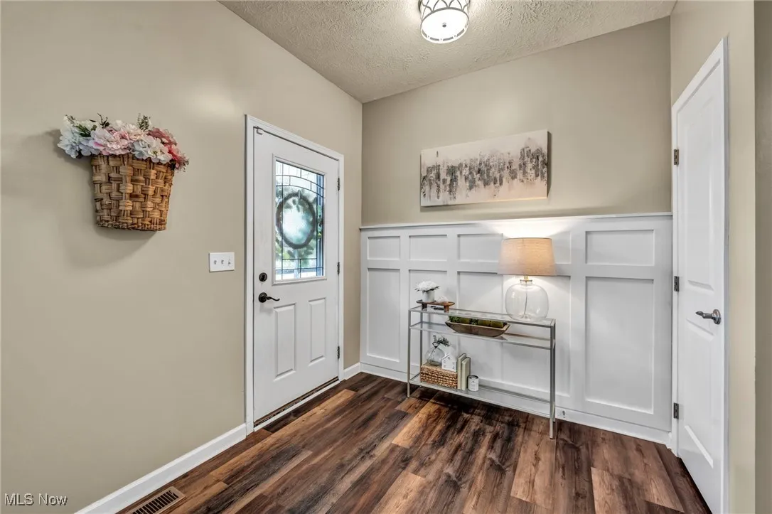 Entrance foyer with a textured ceiling, dark wood finished floors, a wainscoted wall,