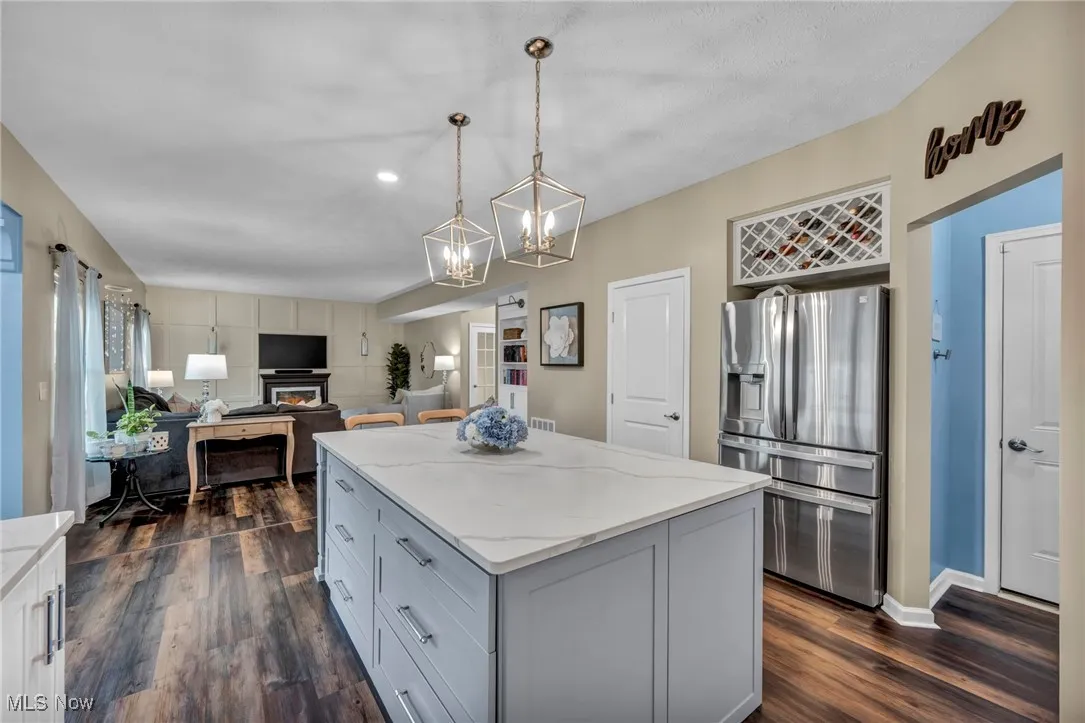 Kitchen with stainless steel fridge with ice dispenser, light stone counters, dark wood finished floors, a center island,