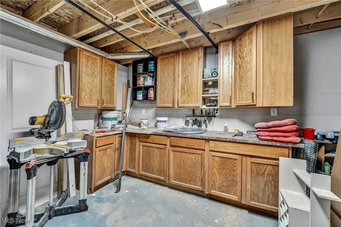 work room in basement with open shelves, unfinished concrete flooring, light countertops, and  cabinetry