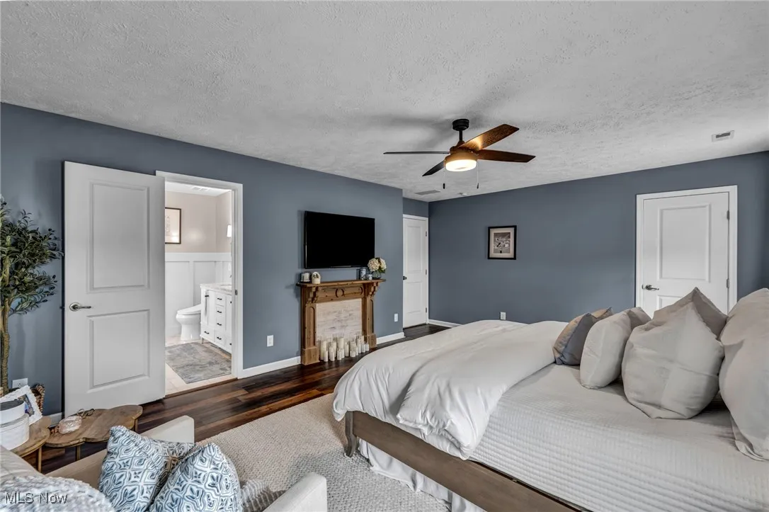 Bedroom featuring wood finished floors, ceiling fan, ensuite bathroom, and a textured ceiling