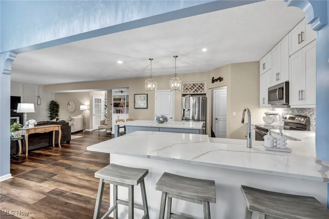 Kitchen featuring a peninsula, appliances with stainless steel finishes, recessed lighting, white cabinetry, and light stone countertops and island
