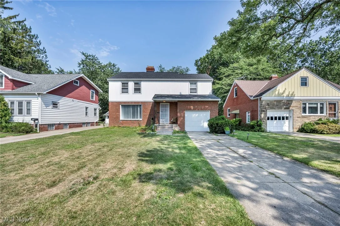 Traditional-style house featuring concrete driveway, brick siding, a chimney, a front lawn, and a garage