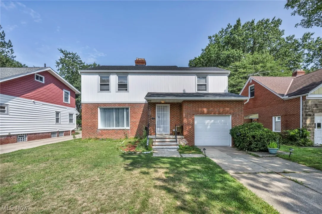 Traditional home featuring concrete driveway, brick siding, a chimney, and a front yard