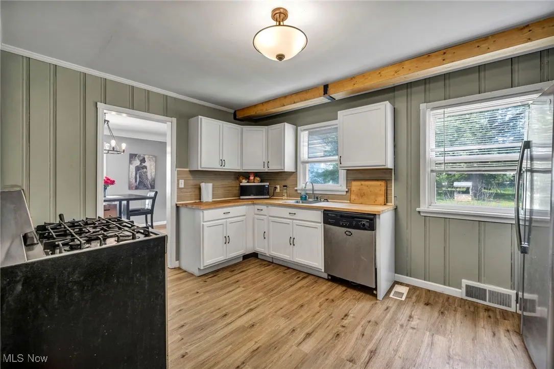 Kitchen featuring light wood finished floors, appliances with stainless steel finishes, white cabinetry, a chandelier, and ornamental molding