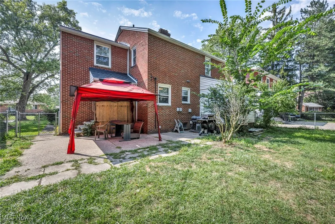 Rear view of house with a gate, brick siding, a patio area, a chimney, and a gazebo