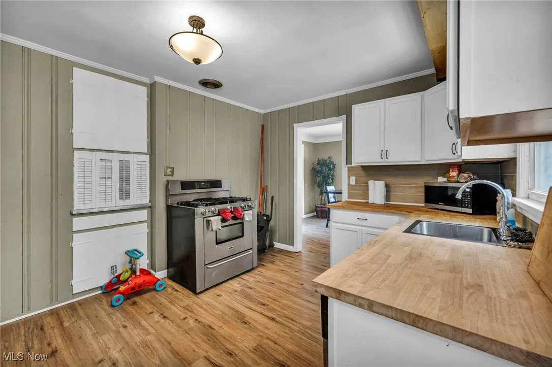 Kitchen with crown molding, appliances with stainless steel finishes, wood counters, white cabinets, and light wood finished floors