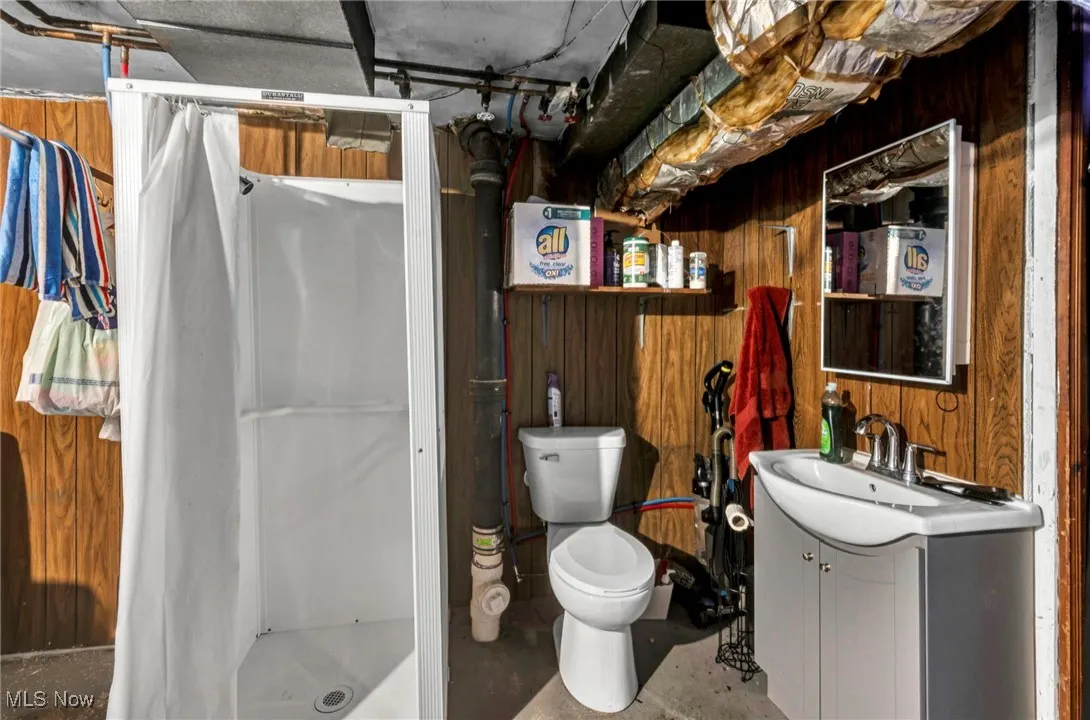 Full bathroom featuring wooden walls, vanity, a shower stall, and concrete floors
