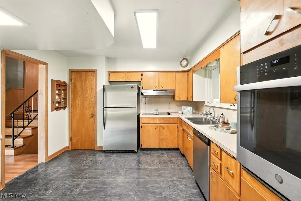 Kitchen with appliances with stainless steel finishes, light countertops, stone finish flooring, decorative backsplash, and under cabinet range hood