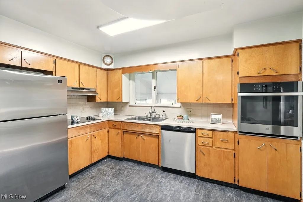 Kitchen featuring stainless steel appliances, backsplash, light countertops, and under cabinet range hood