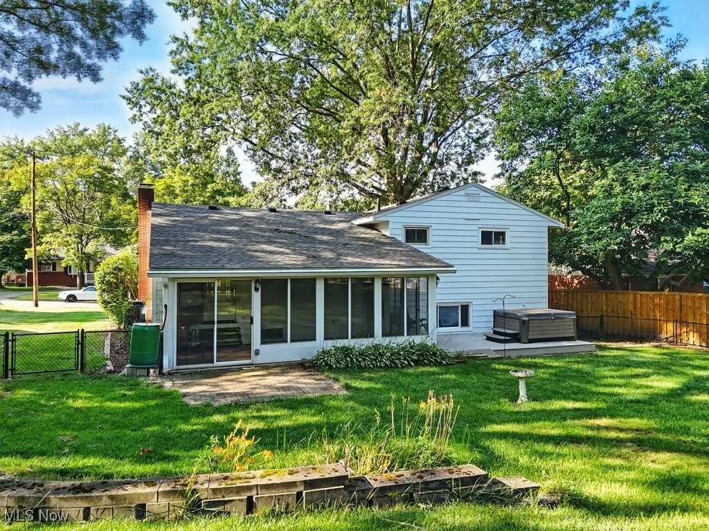 Rear view of property featuring a hot tub, a fenced backyard, a chimney, a sunroom, and a patio area