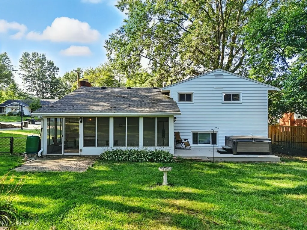 Back of property featuring a hot tub, a patio area, a sunroom, and a chimney