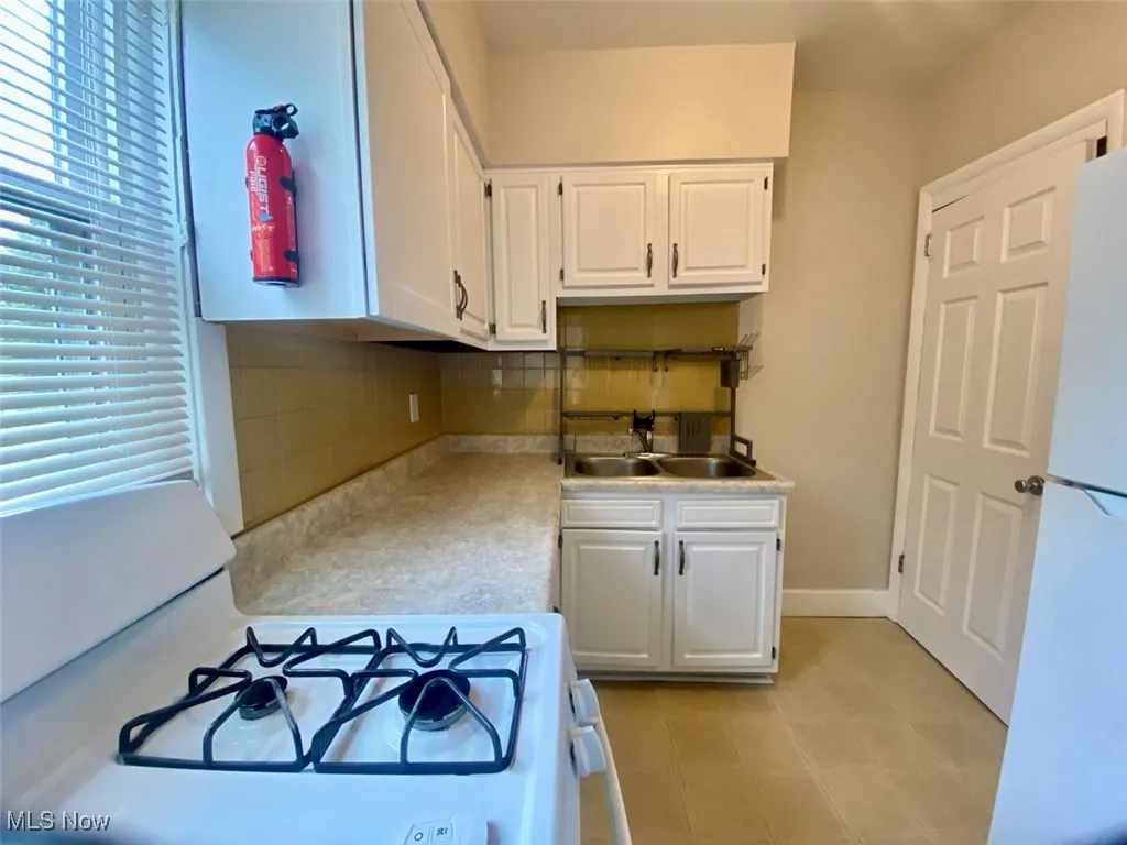 Kitchen with white appliances, decorative backsplash, white cabinetry, and light countertops