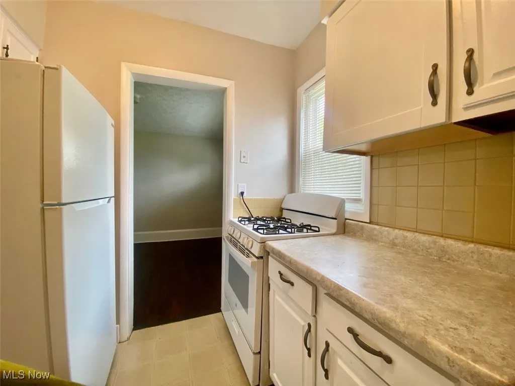 Kitchen featuring white appliances, light countertops, decorative backsplash, and white cabinets
