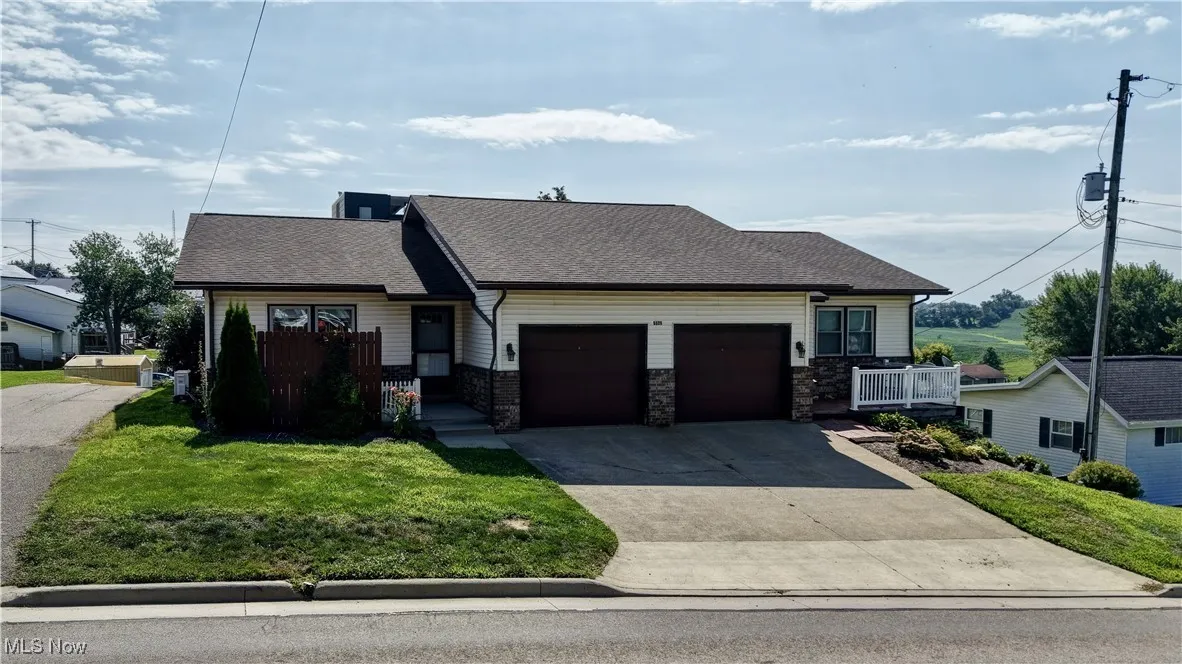View of front of house with a shingled roof, stone siding, an attached garage, concrete driveway, and a front yard