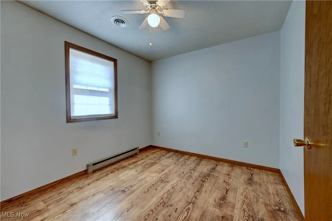 Unfurnished room featuring baseboard heating, light wood-style flooring, and a ceiling fan