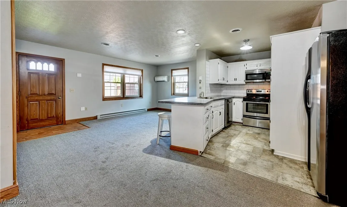 Kitchen with a peninsula, light carpet, appliances with stainless steel finishes, backsplash, and white cabinets