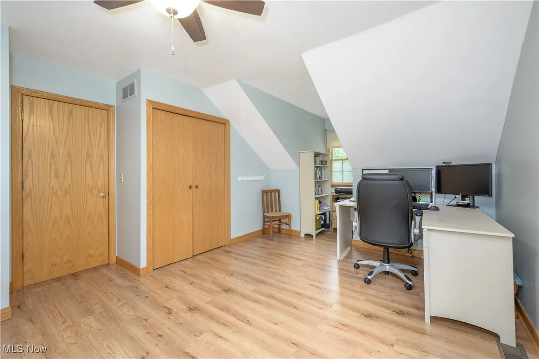 Office area with light wood finished floors, vaulted ceiling, and a ceiling fan