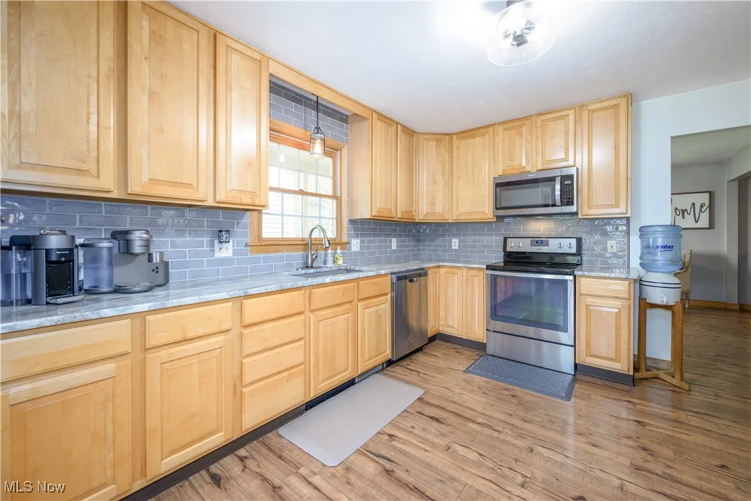 Kitchen with light brown cabinets, stainless steel appliances, decorative backsplash, and light wood-style floors