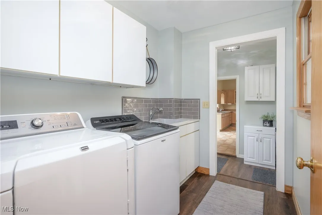 Laundry area with dark wood-type flooring, cabinet space, and washing machine and clothes dryer