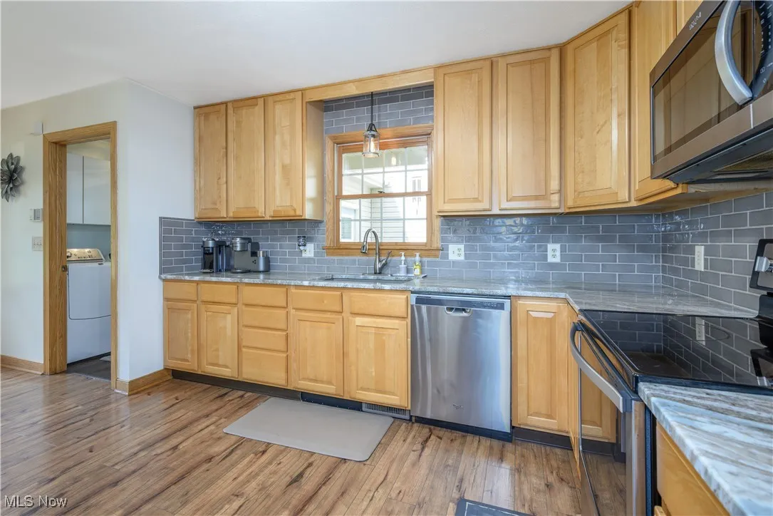 Kitchen featuring stainless steel appliances, backsplash, light wood-style floors, washer / dryer, and light stone counters