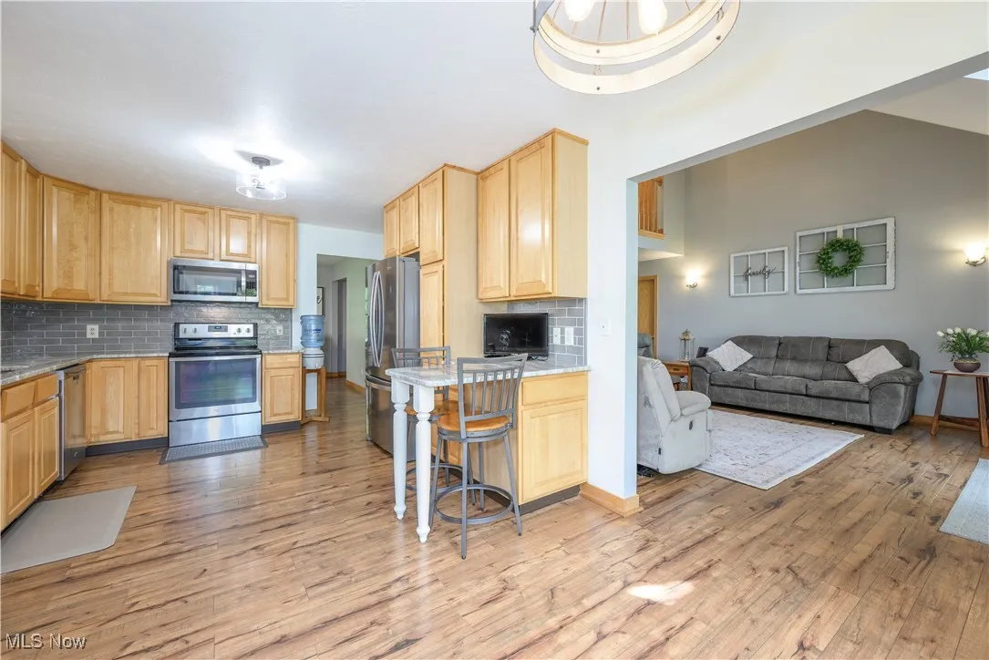 Kitchen with light brown cabinets, tasteful backsplash, appliances with stainless steel finishes, and open floor plan