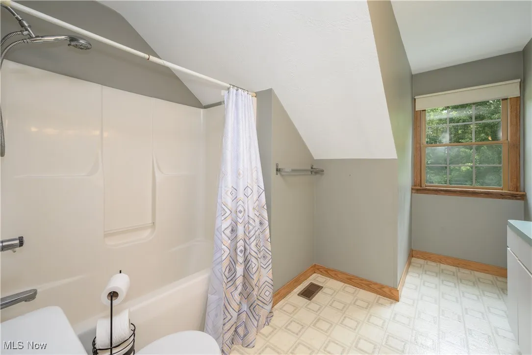 Full bathroom with tile patterned floors, shower / bath combo with shower curtain, vaulted ceiling, and vanity